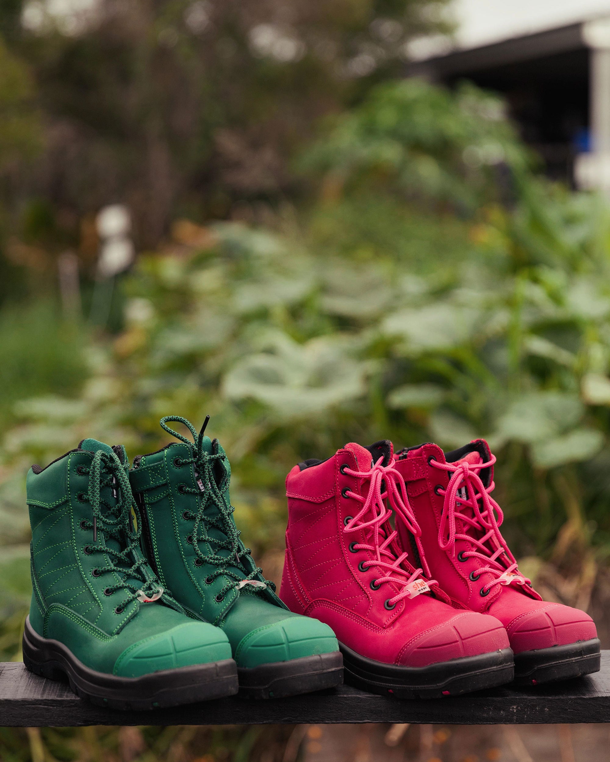 Two pairs of jade green and hot pink safety boots rest on a garden bench