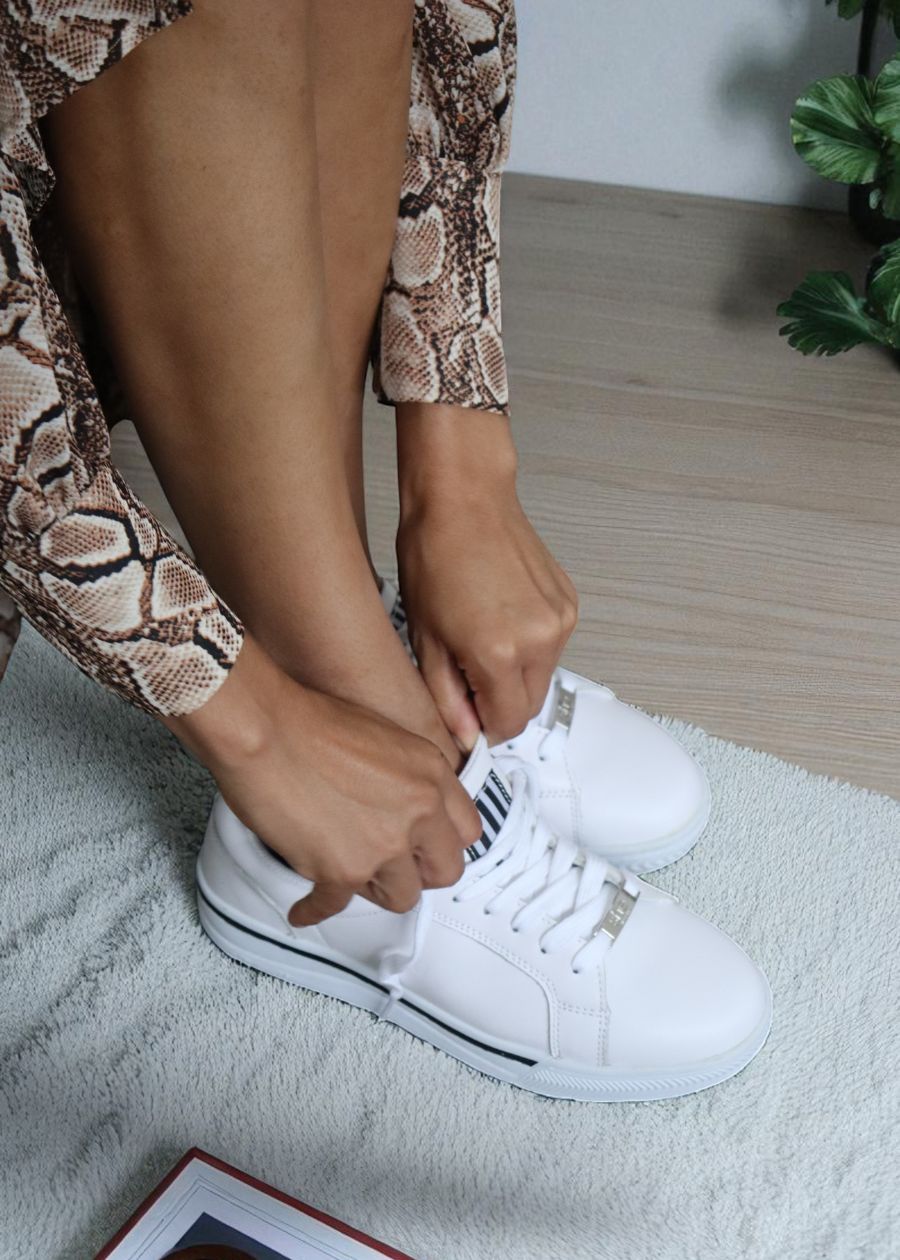 Person tying white sneakers on a light-colored rug