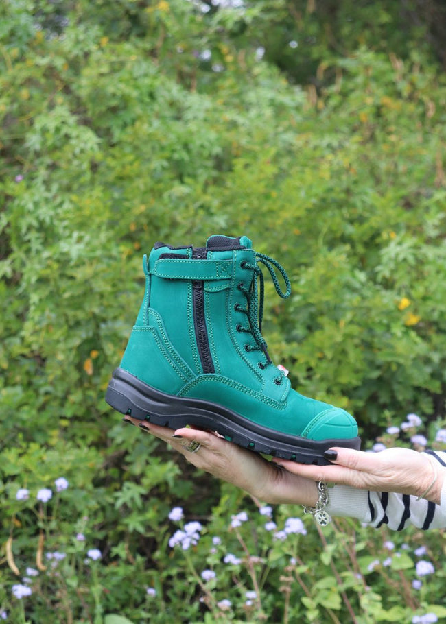 Size view of jade green zip-up safety boots, with bush in background.
