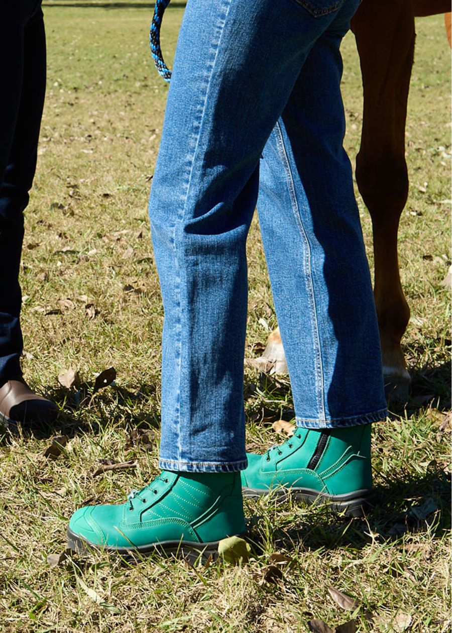 Person wearing green lace-up safety boots in grass.