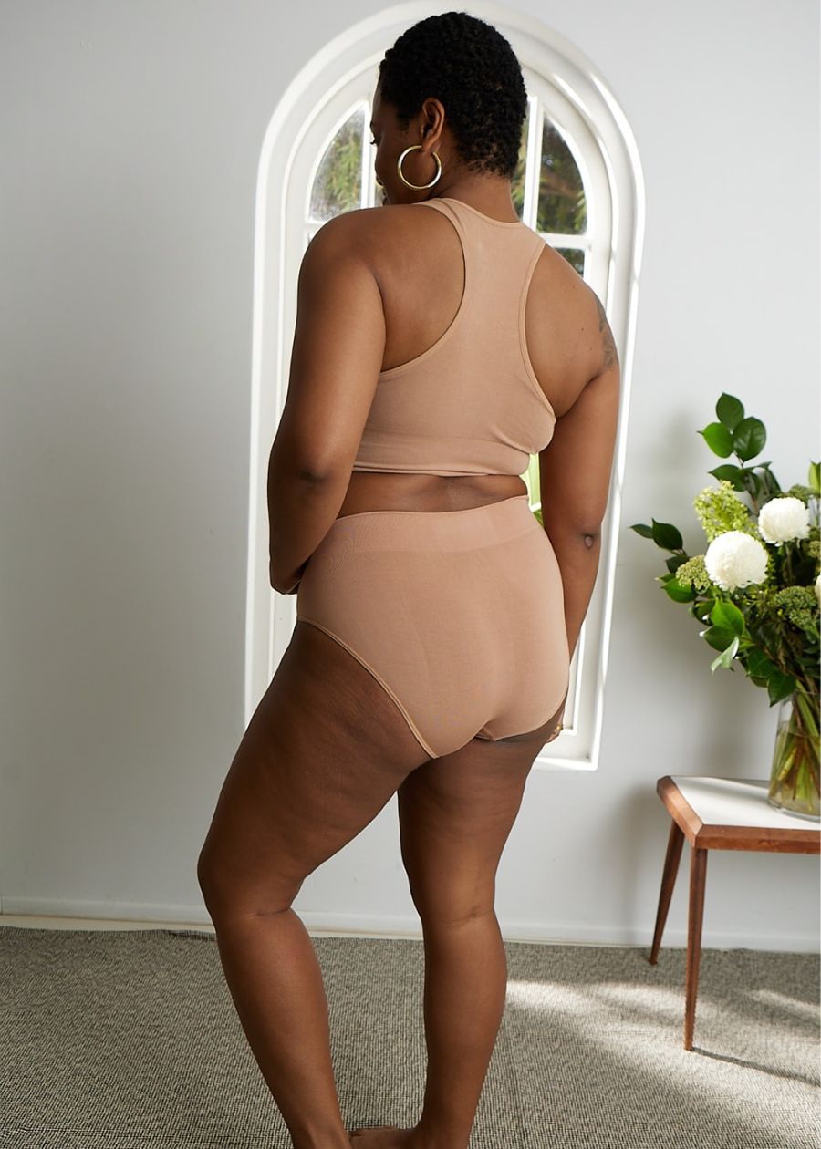 Rear view of woman in a nude or flesh tone racerback crop top bra and full coverage briefs made of stretchy organic bamboo.