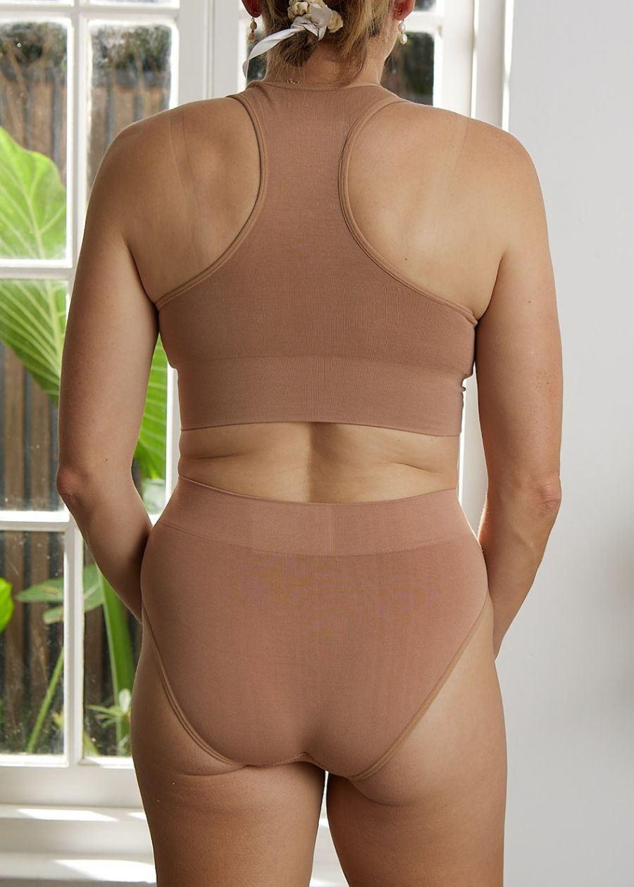 Rear view of woman wearing a nude or flesh tone racerback crop top bra and high-cut briefs made of stretchy organic bamboo.