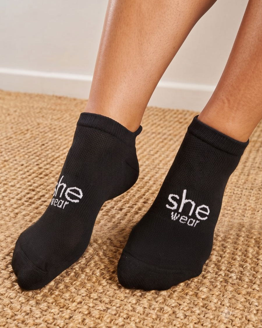 a pair of feet wearing a pair of women's black ankle length socks with a white she wear logo on the top