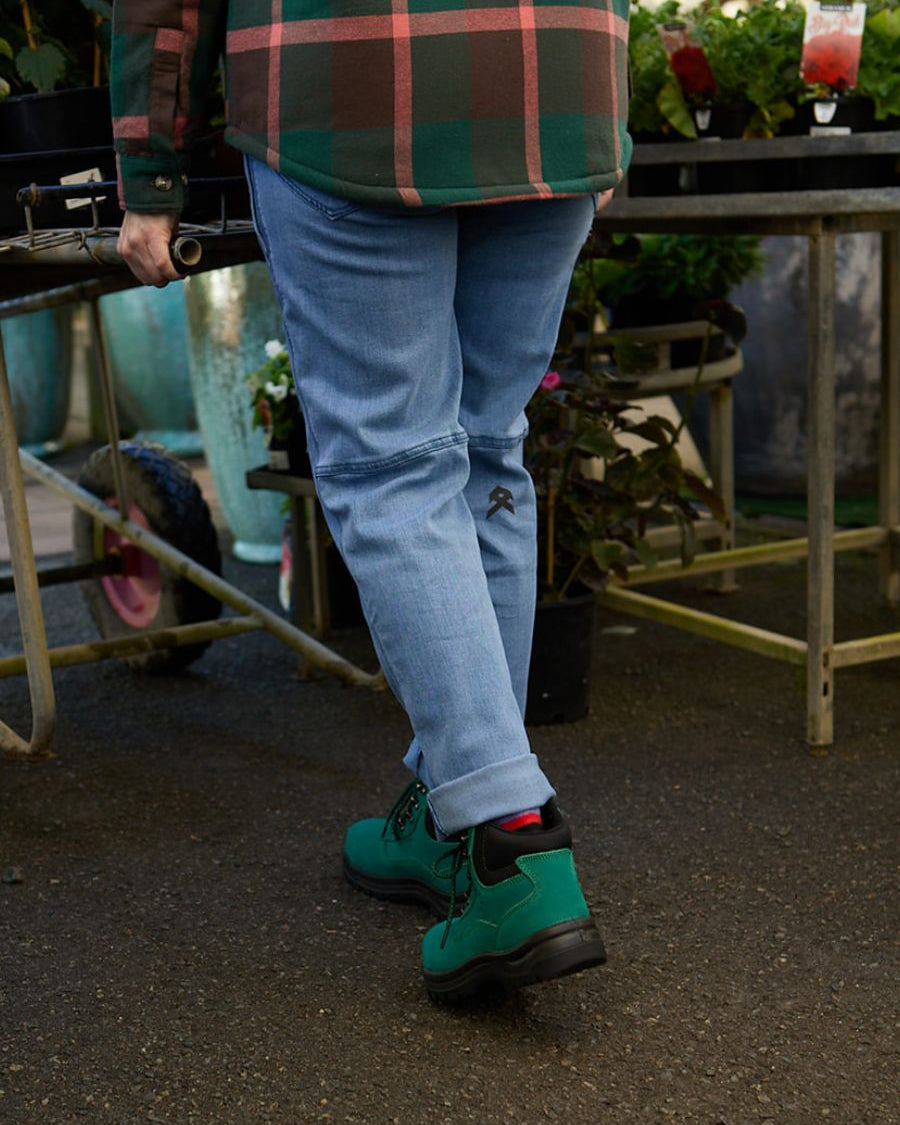 Back view of woman pushing trolley of flowers in green ankle height wide-fit steel cap boots.