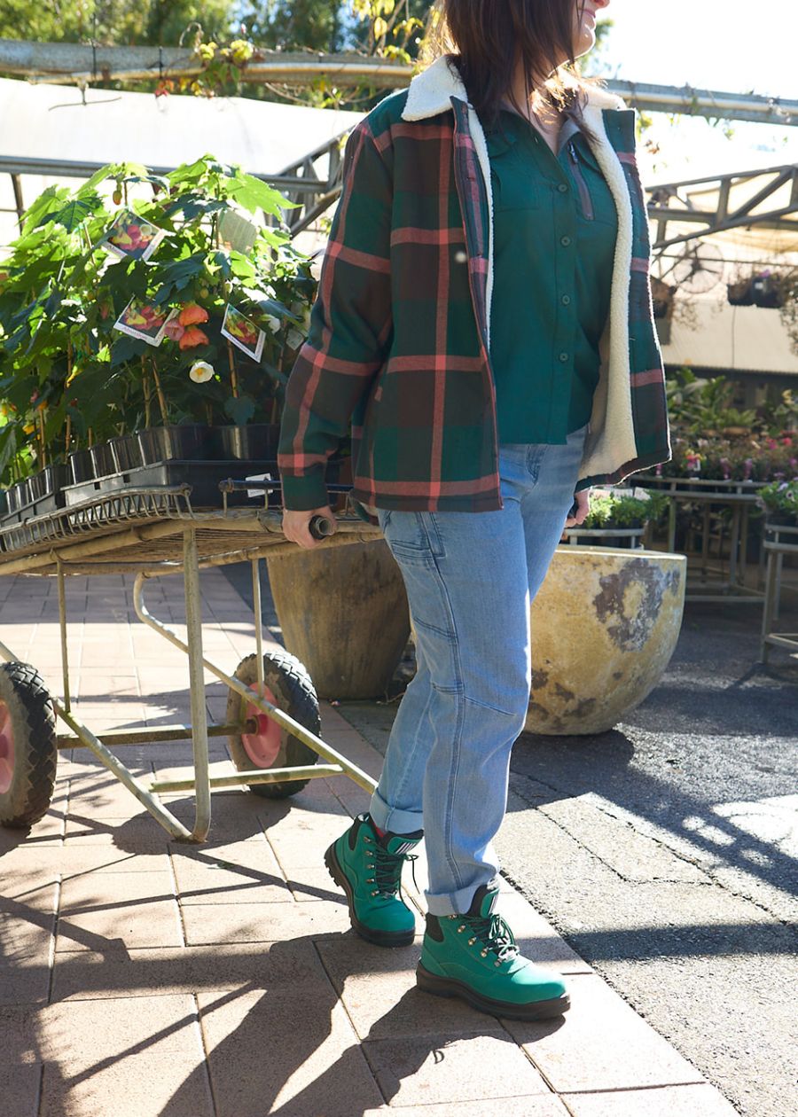 Woman towing trailer of flowers in green sherpa hoodie with red accents.