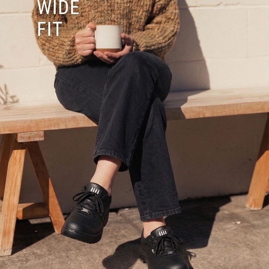 Lady sat down with a mug wearing wide fit black working shoe