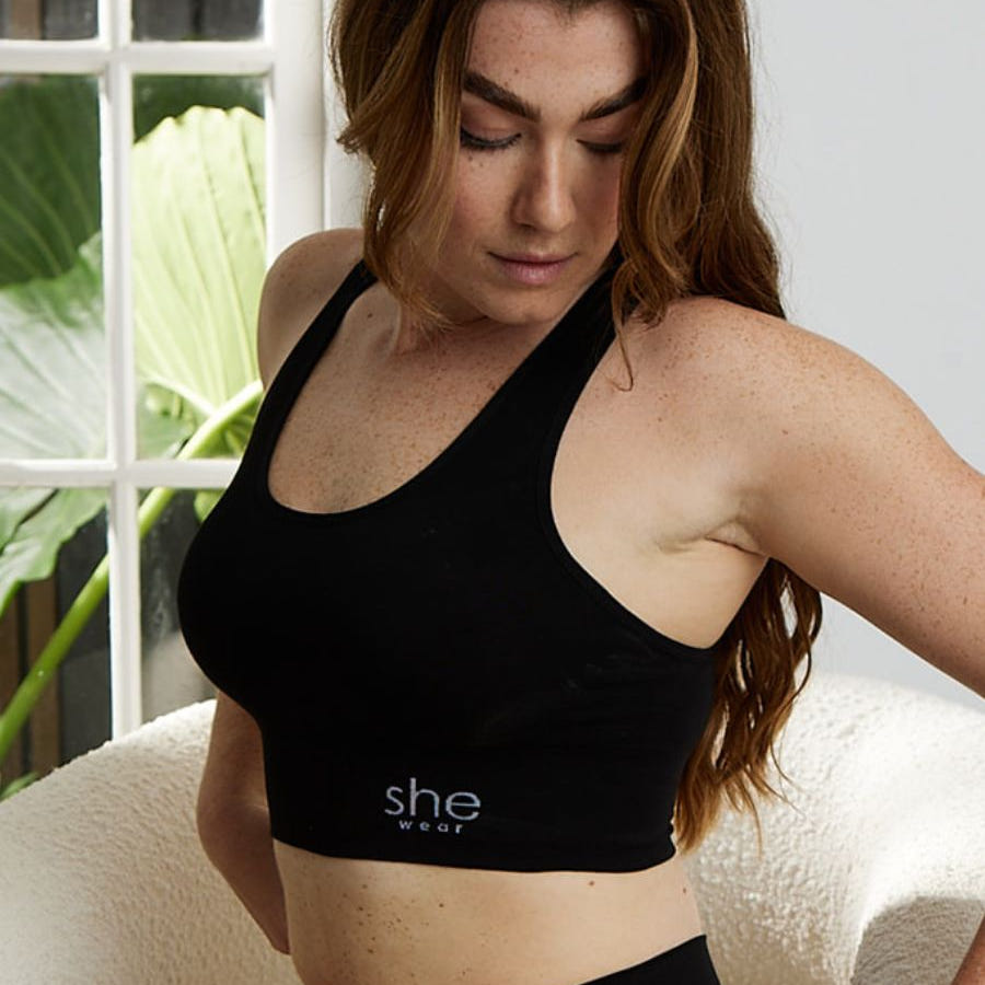A seated woman in a comfortable black racerback crop top bra and briefs made of organic bamboo by an Australian company.