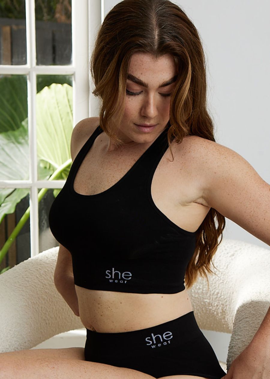 A seated woman in a comfortable black racerback crop top bra and briefs made of organic bamboo by an Australian company.