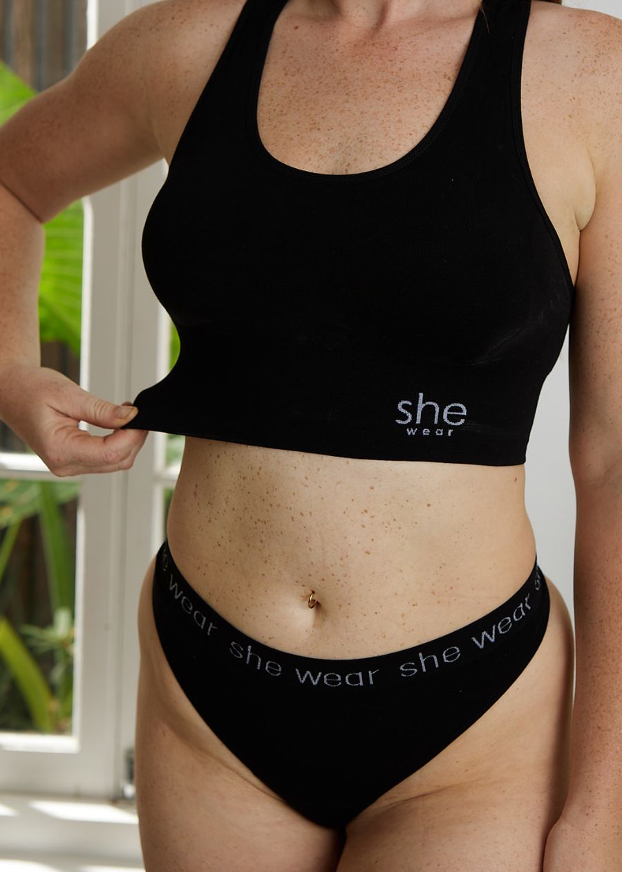Interior shot of a woman showing how stretchy her black organic bamboo crop top bra is. She is wearing matching black briefs.