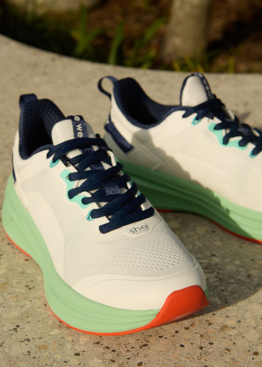 White walking shoe with navy laces, and a green and orange sole