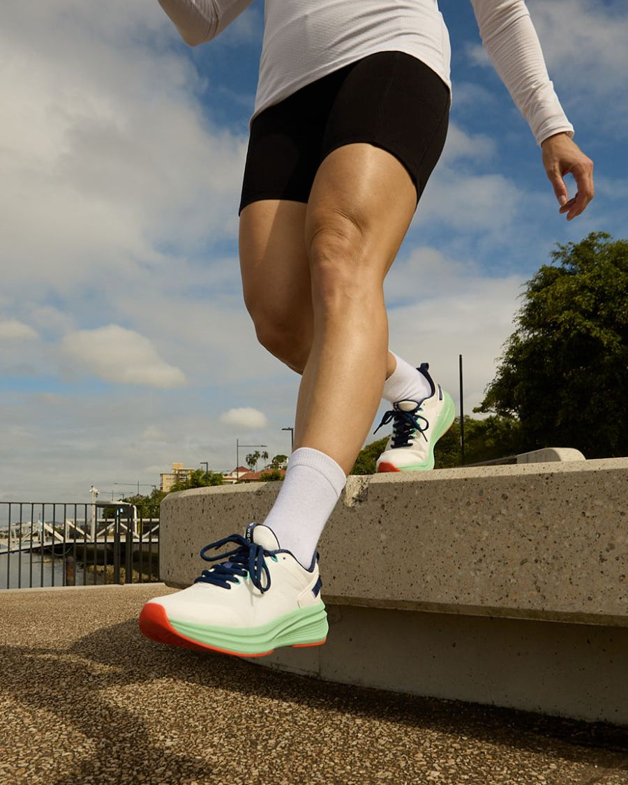 Woman stepping down from stone ledge in black and mint walking shoes.
