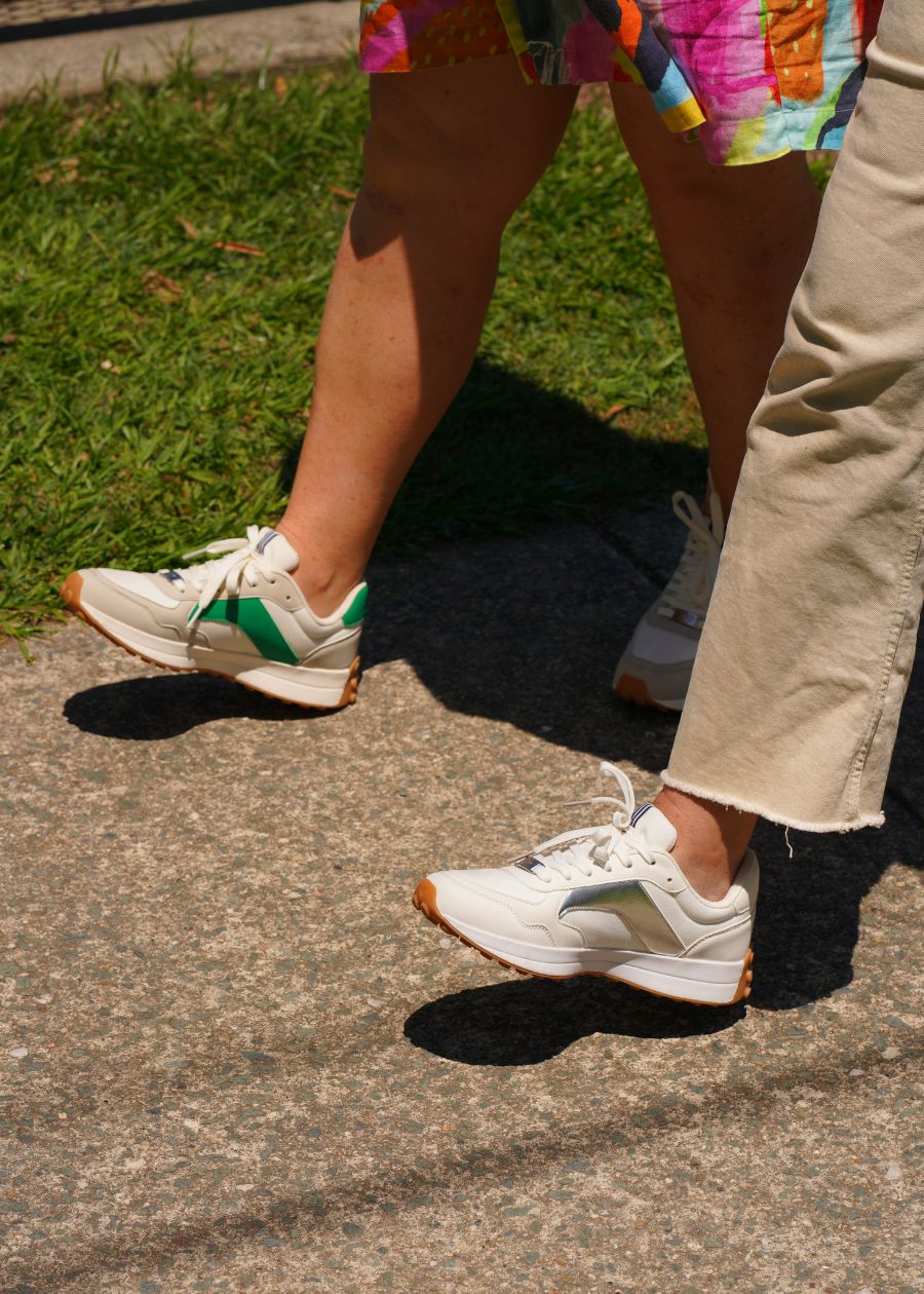 Two women walking wearing fashion sneakers in different colours - one green, one silver