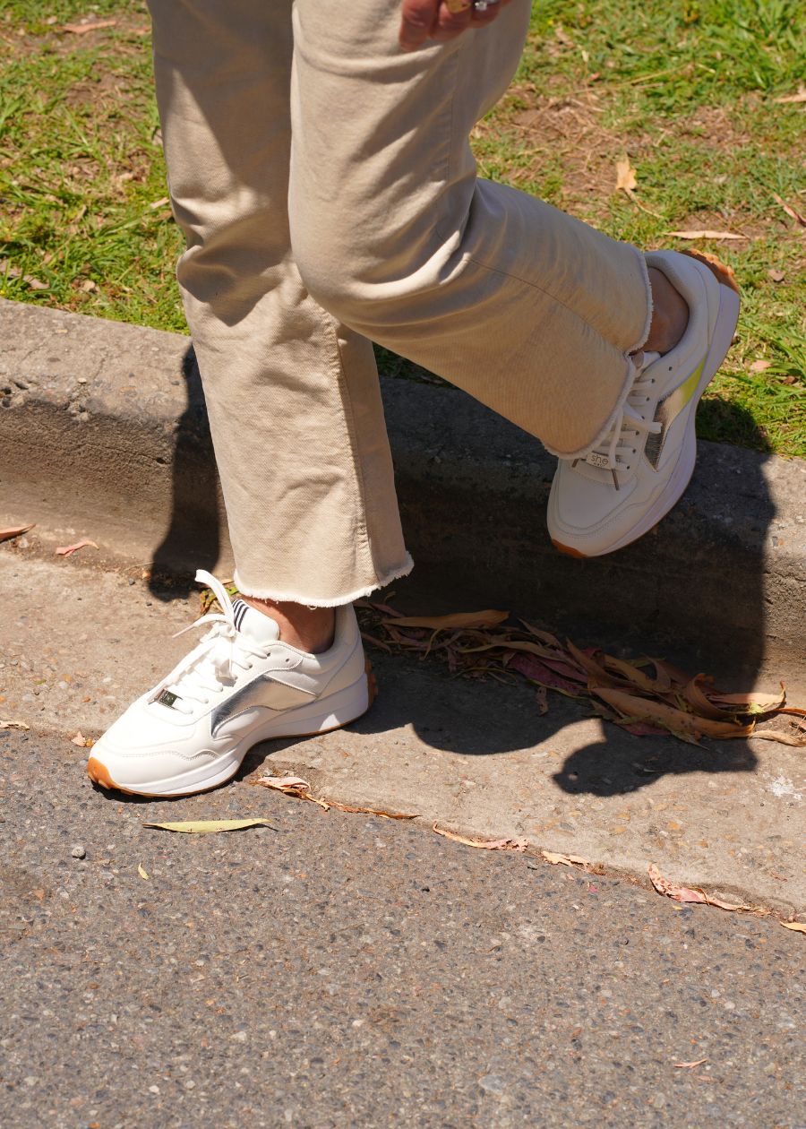 A woman wears tan jeans with white and silver sneakers