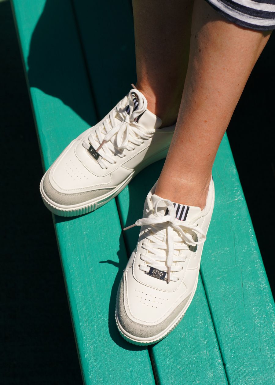 A view of a pair of white vegan sneakers with Breathable mesh lining in white and grey standing on a green bench