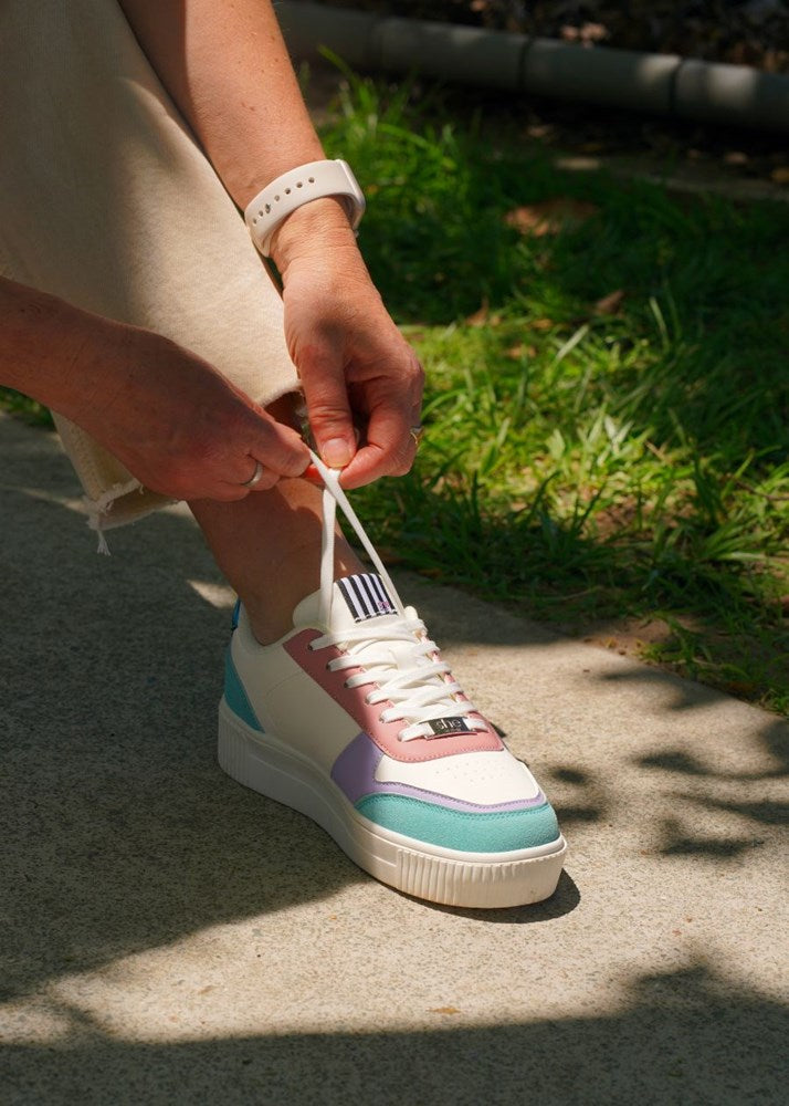 A woman ties the laces on her colourful sneaker on a garden path