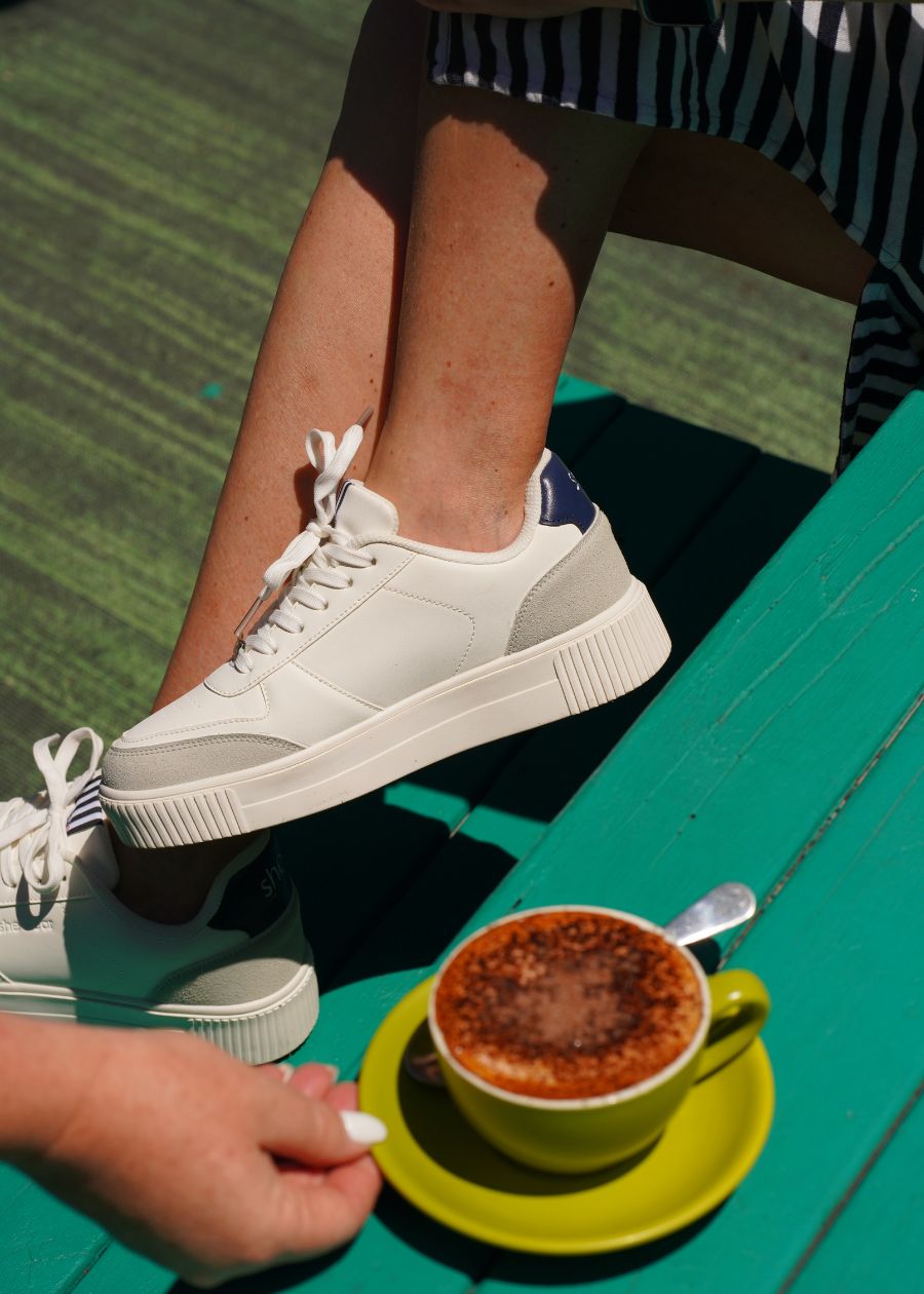 White, navy and grey platform sneakers with a padded heel collar for comfort shown behind a cup of coffee