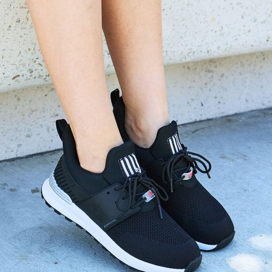 Side view of black active sneakers, with white soles. On a stone background.