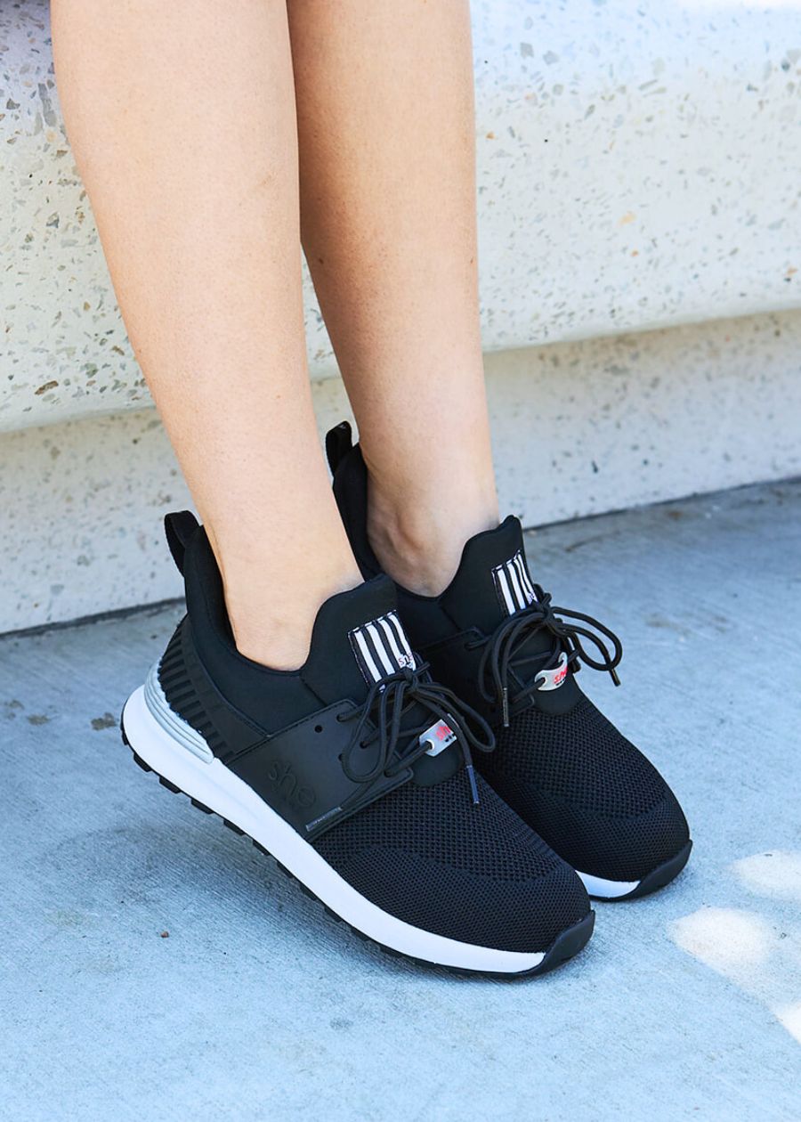 Side view of black active sneakers, with white soles. On a stone background.