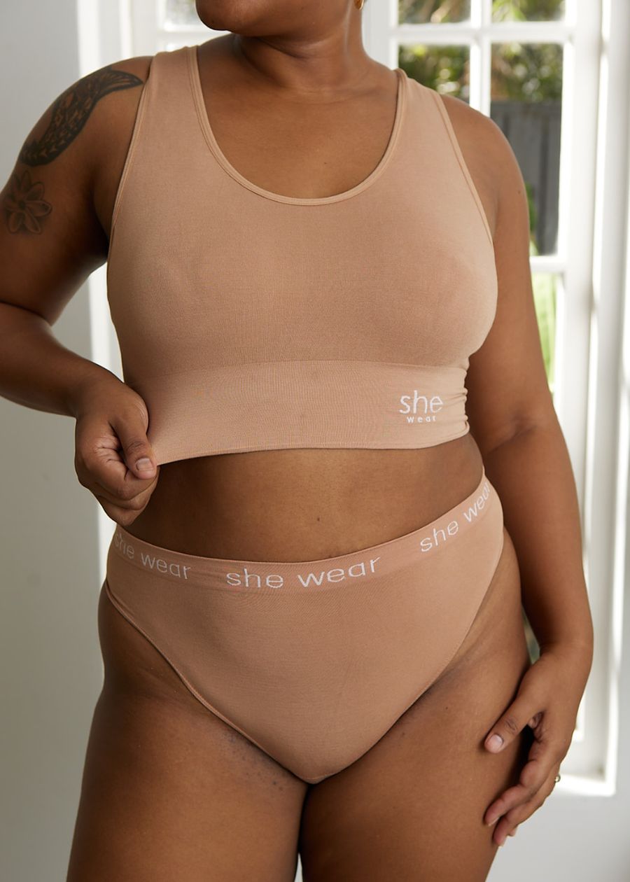 A woman showing how stretchy her nude or flesh tone organic bamboo crop top bra is. She’s wearing matching briefs.