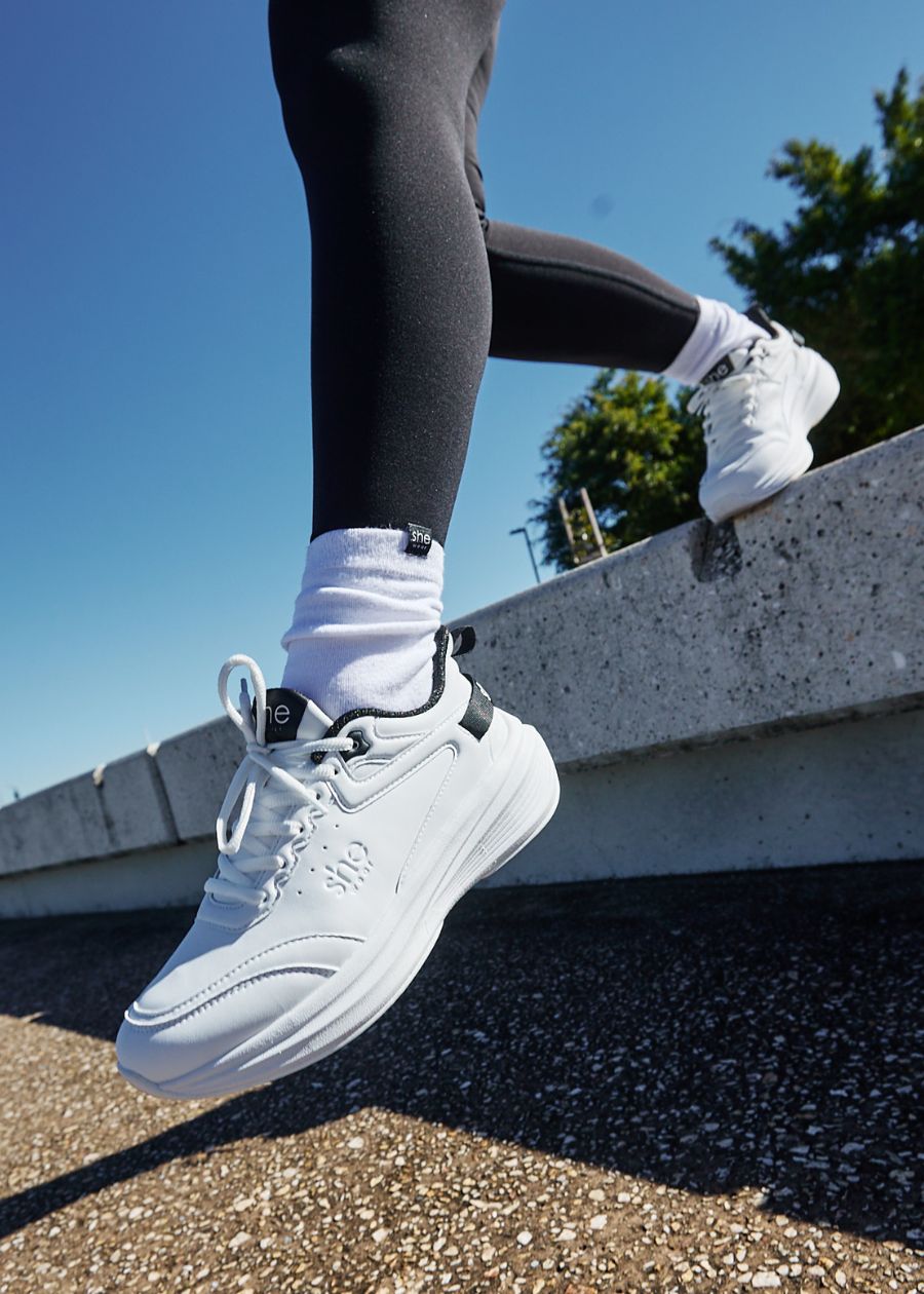 Woman taking a step off a ledge wearing white walking sneaker