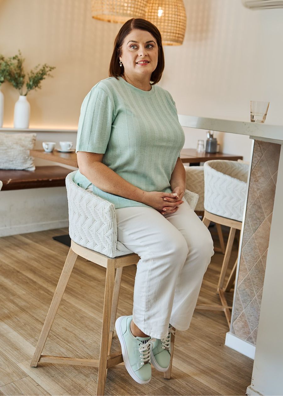Woman wearing mint lace-up sneakers, white white sole, while sitting on a bar stool.