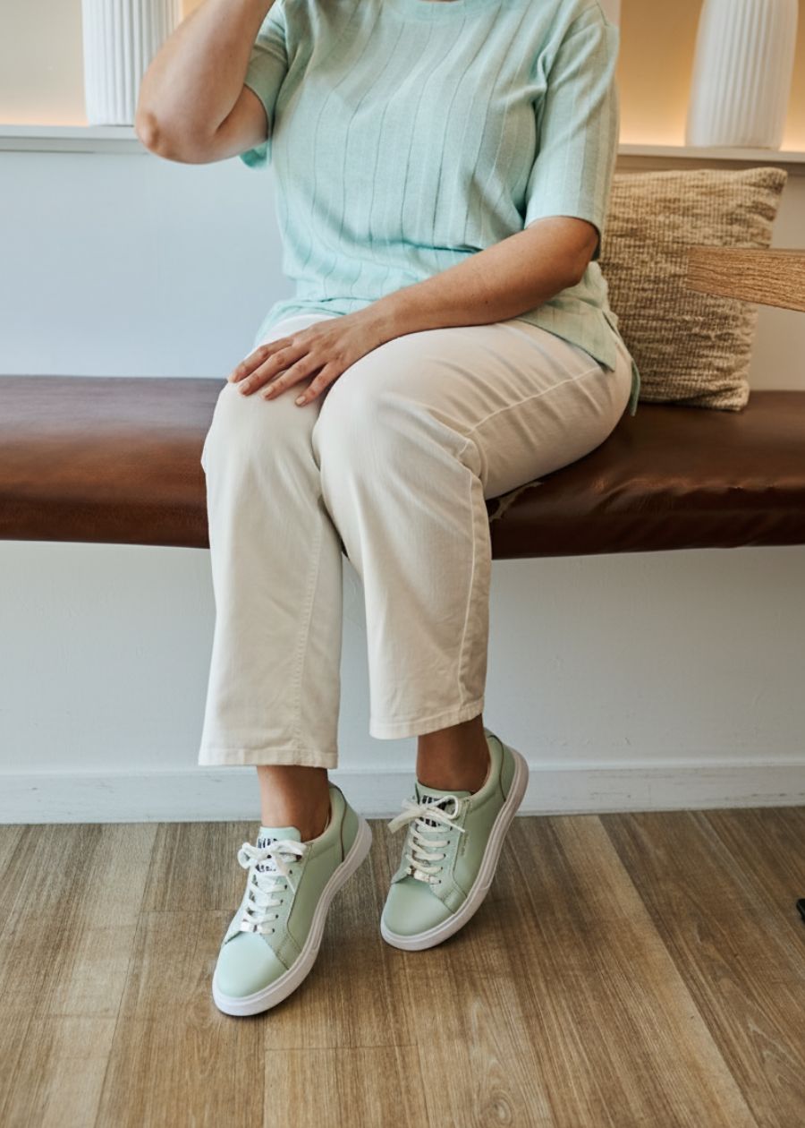 Woman in mint shirt, and white pants wearing mint coloured dress sneakers that feature a white sole.
