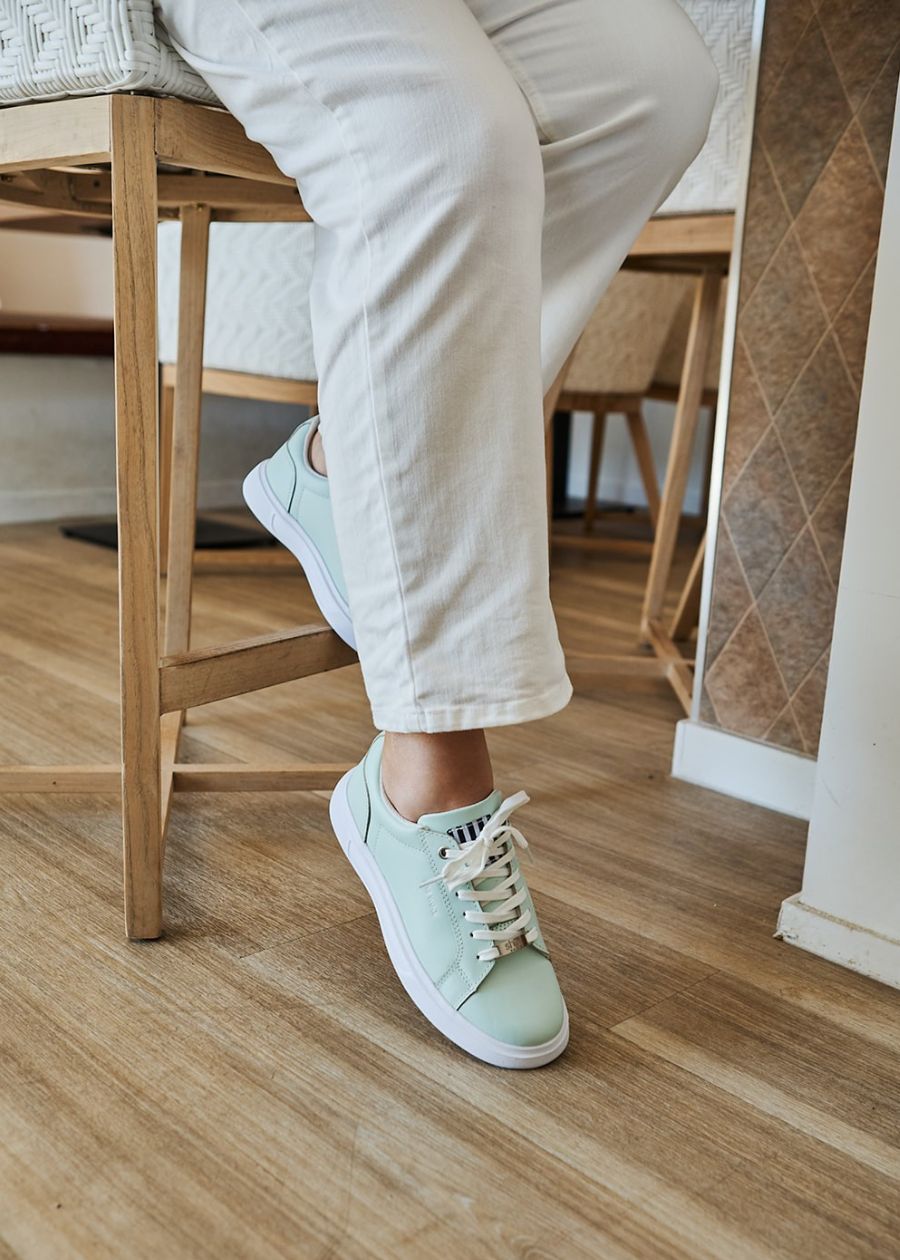 Side view of woman wearing mint lace-up sneaker with white sole. Woman is on a stool.