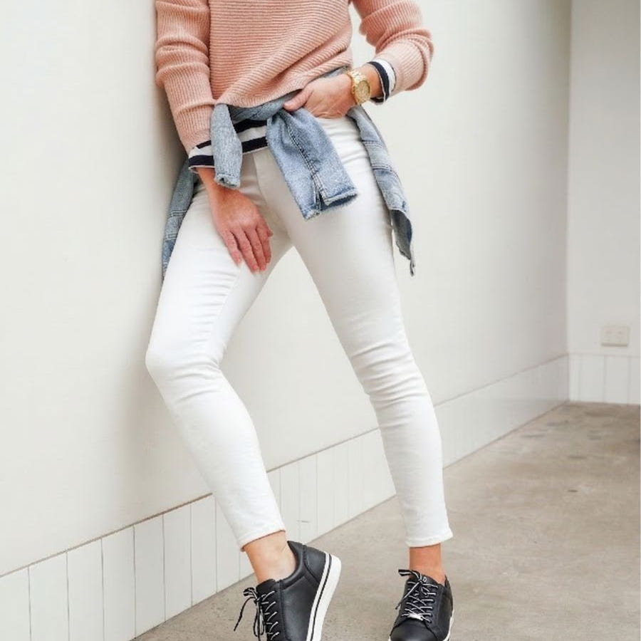 Woman leaning against a white wall wearing black and white supportive sneakers.