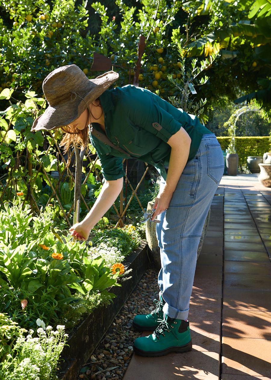 Woman gardening in green UPF rated button up shirt with sleeves rolled up and buttoned.