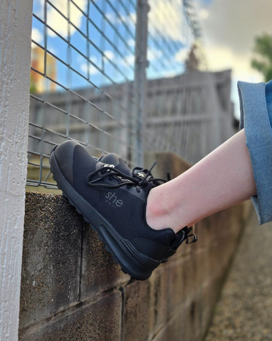 Feet braced against a stone wall, wearing black safety sneakers