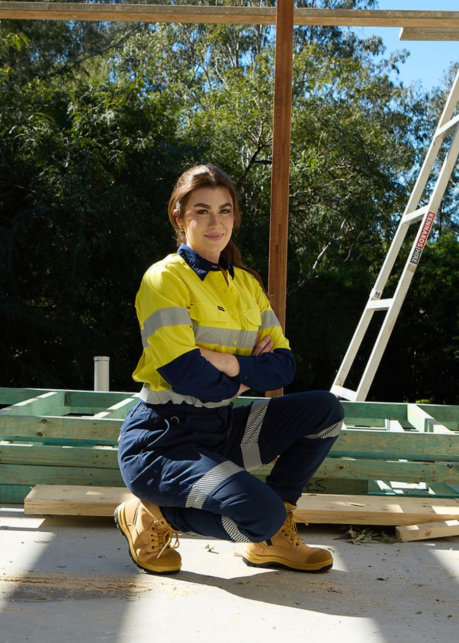 Woman on a construction site is squatting while wearing reflective navy work pants.