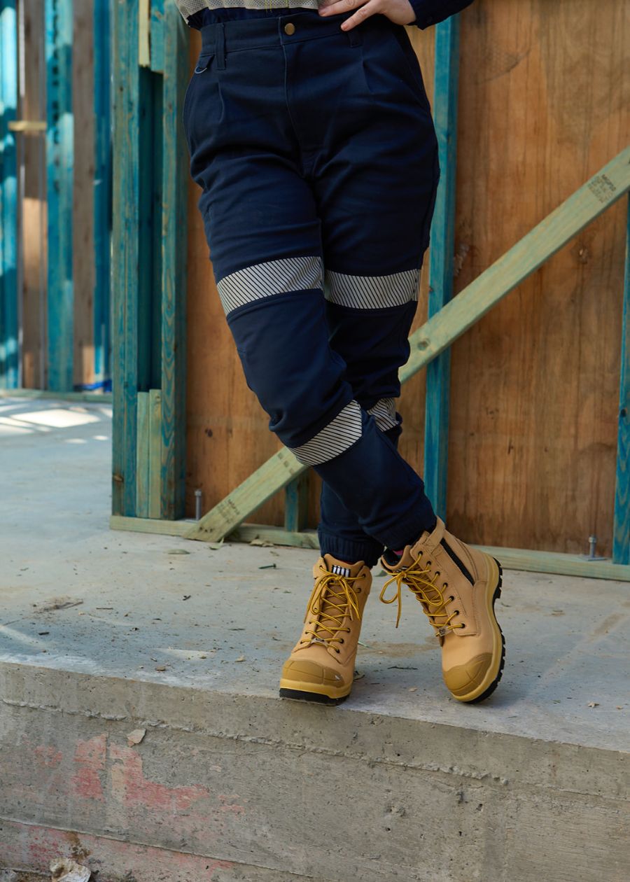 Woman wearing high wasted, navy work pants, with two high-vis stripes.