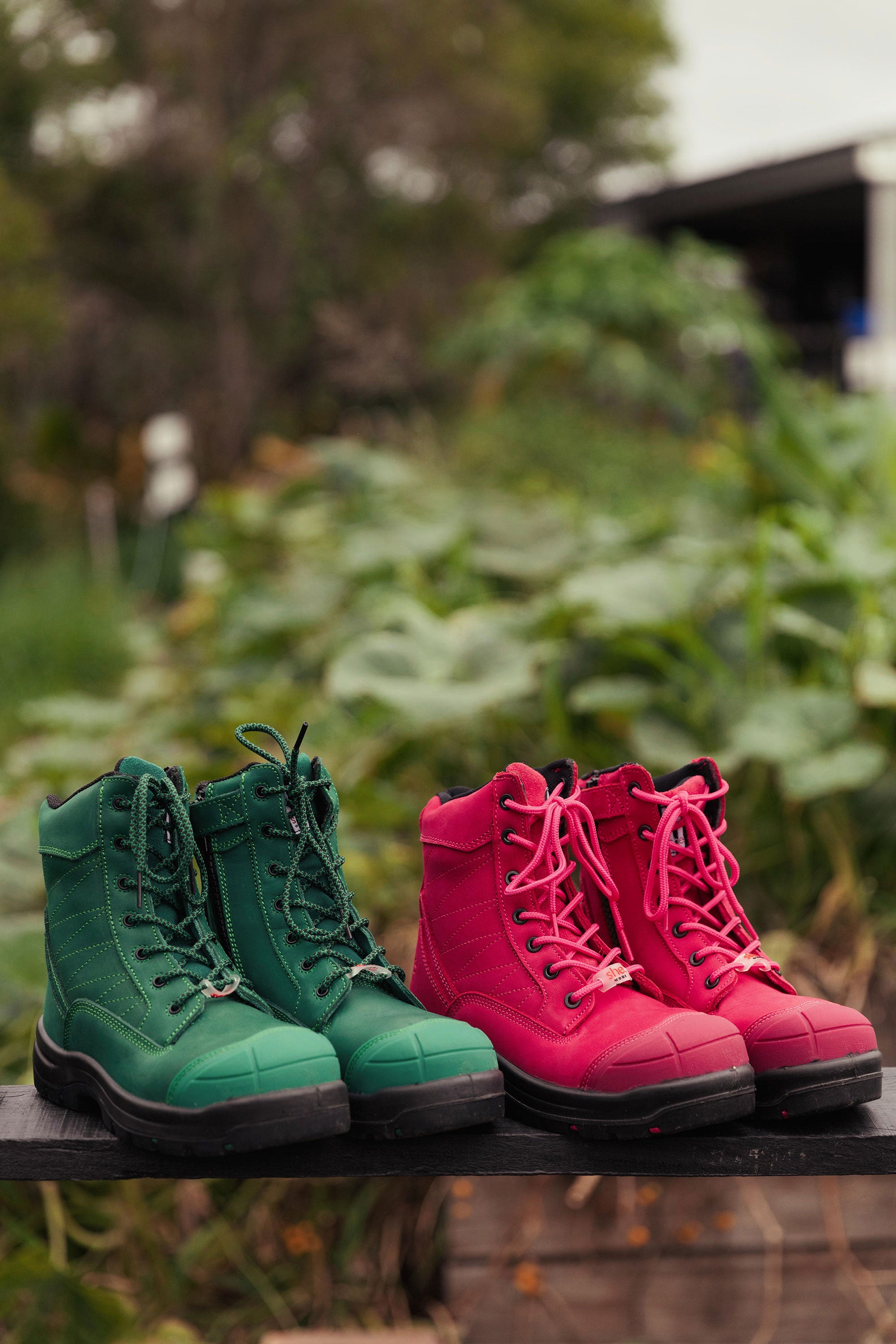 Two pairs of jade green and hot pink safety boots rest on a garden bench