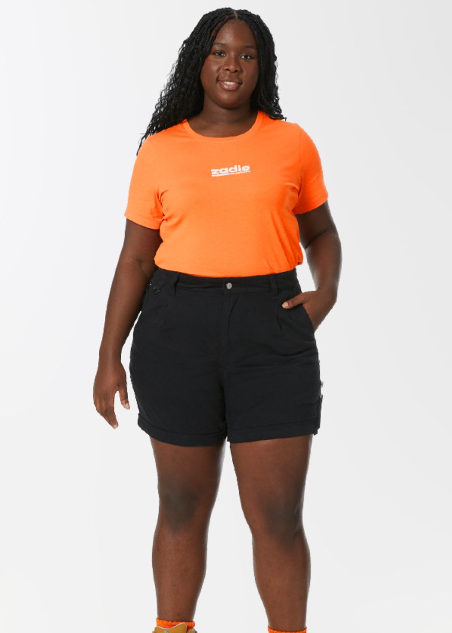 A woman wearing an orange t-shirt and black high-waisted shorts