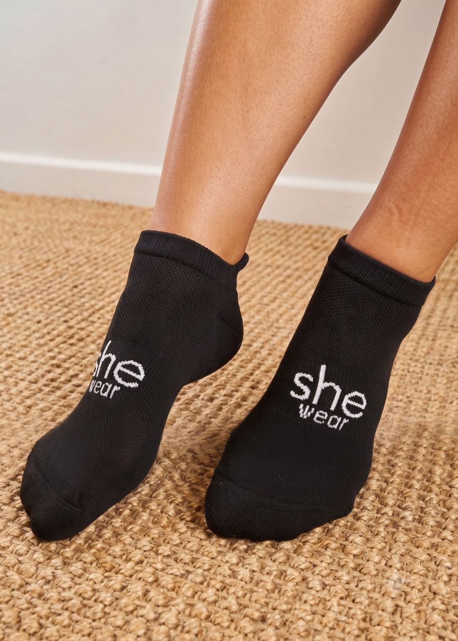 a pair of feet wearing a pair of women's black ankle length socks with a white she wear logo on the top