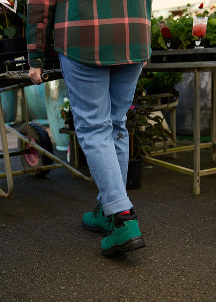 Back view of woman pushing trolley of flowers in green ankle height wide-fit steel cap boots. 