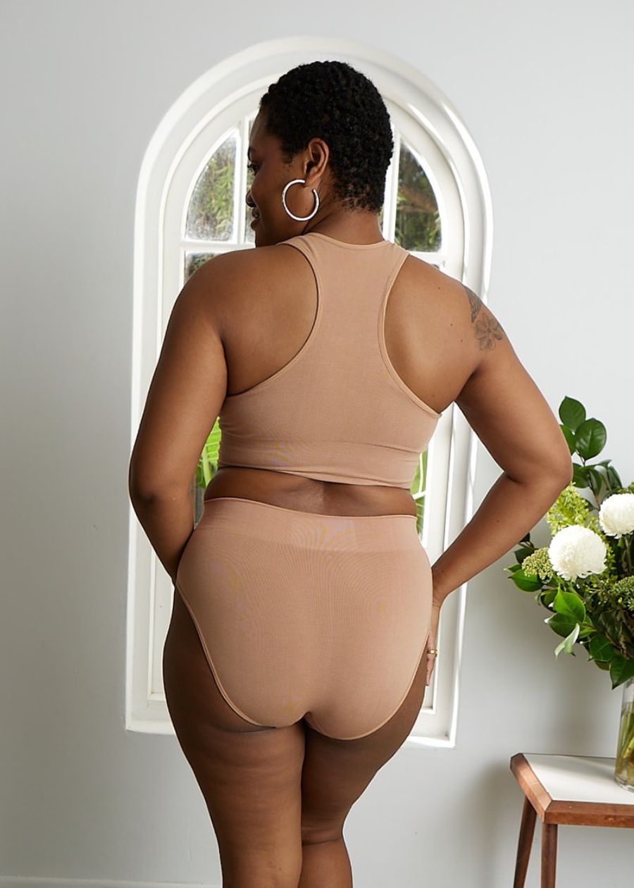 Back view of a woman wearing a seamless beige racerback bra and high-waisted briefs. The stretchy, sculpting fabric offers a smooth and supportive fit