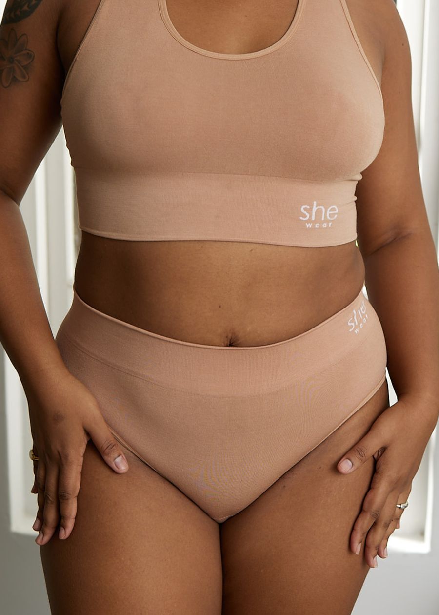 Woman wearing a supportive nude racerback crop top and high-waisted full-coverage briefs.