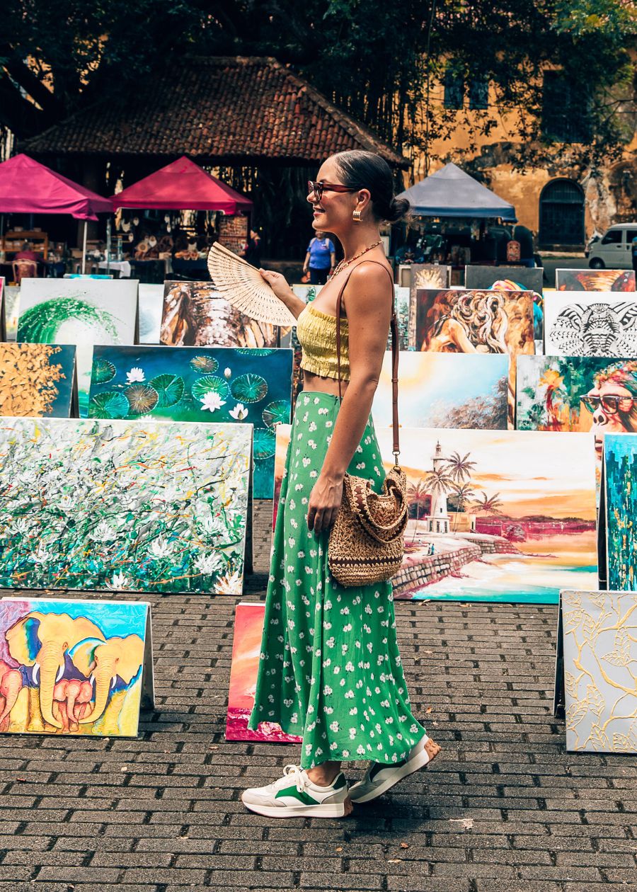 Tourist in front of art work wearing green skirt and white athleisure sneaker with green accent colours. 