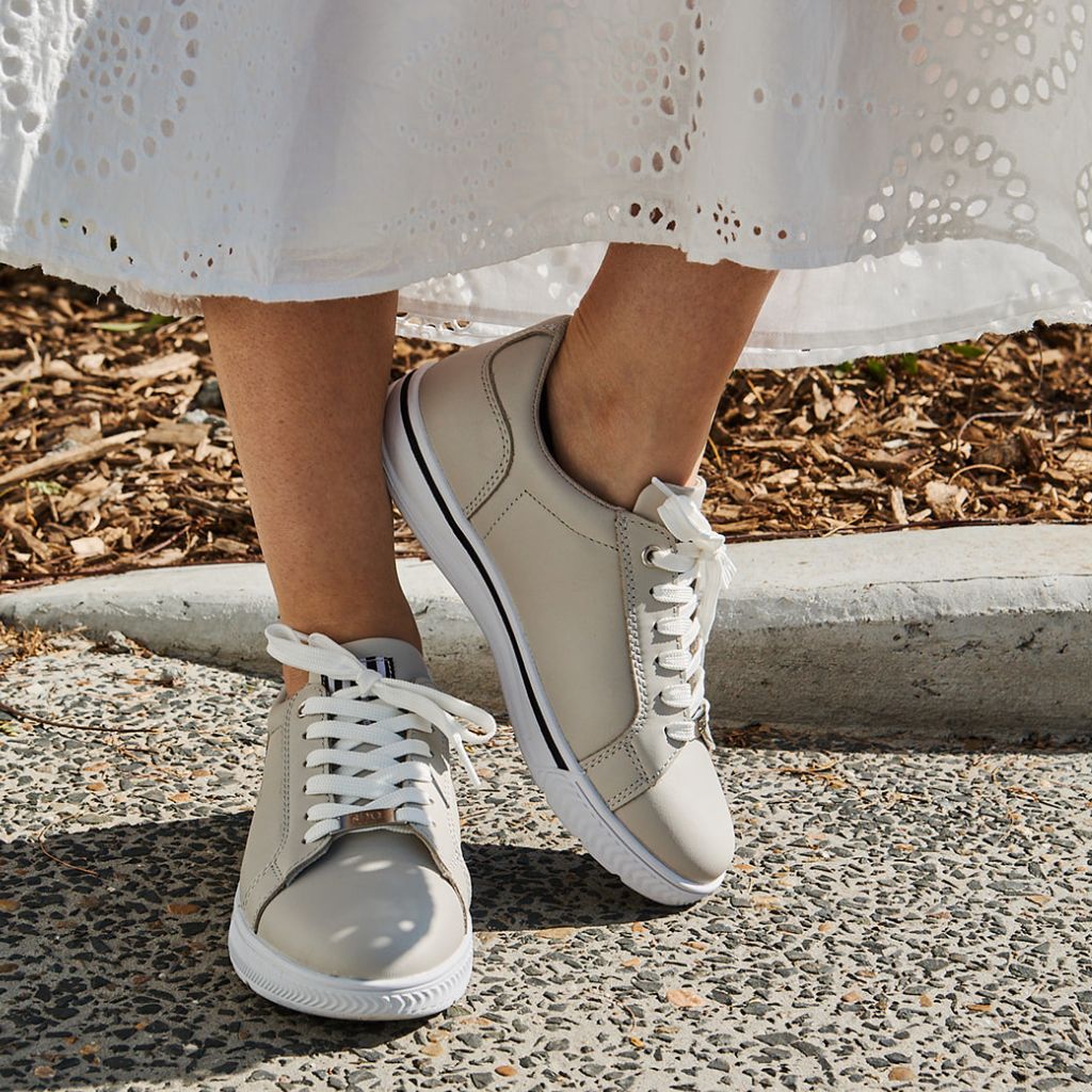 Person wearing tan coloured sneakers, standing on a driveway with a white skirt.