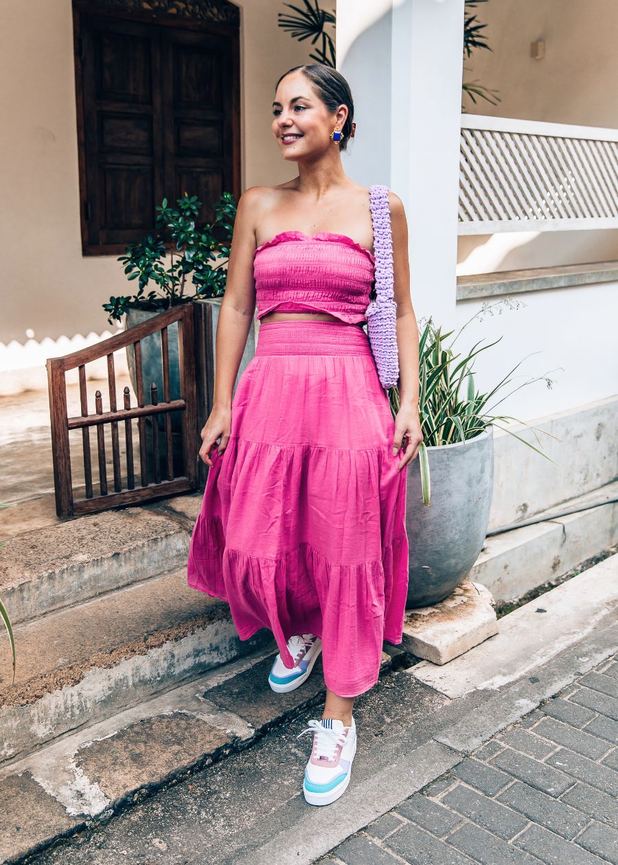 Woman in a pink outfit standing on steps with blue, pink and white Rise sneakers. There are plants and a building in the background
