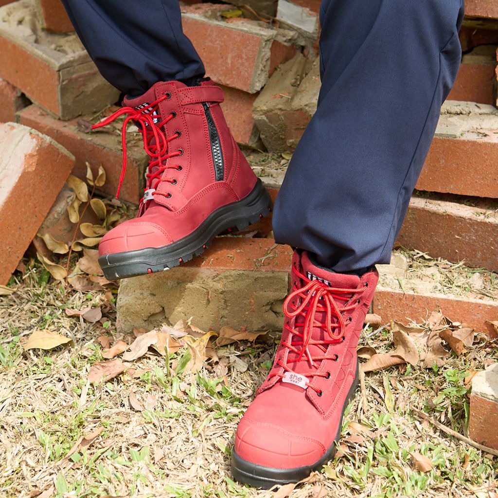 Sitting on a pile of bricks with red lace-up safety boots, featuring a size zip and Velcro strap.