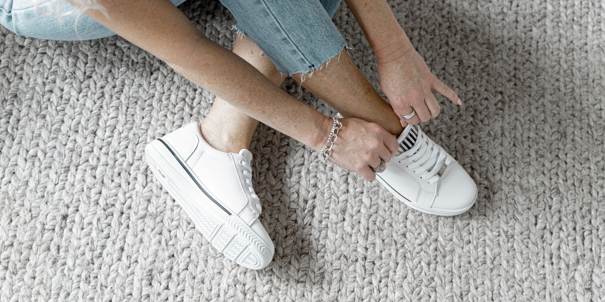 Woman tying up white lace up shoes on grey carpet. 