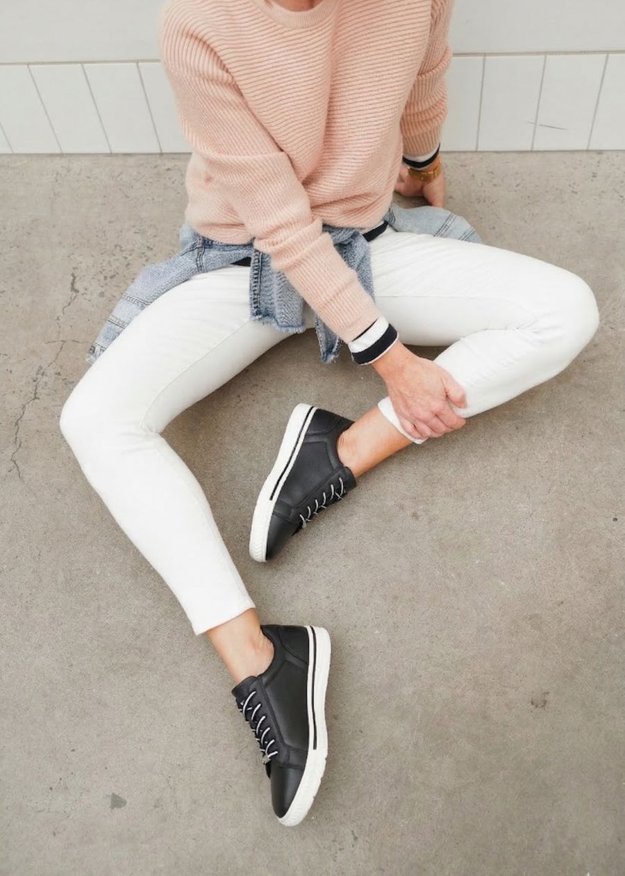 Woman sitting on concrete wearing comfortable black and white sneakers. 