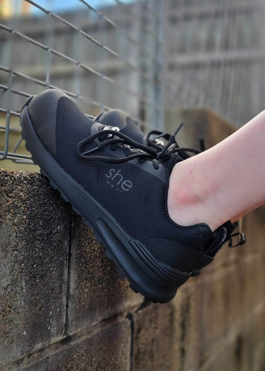 Feet against wall wearing black mesh safety sneakers
