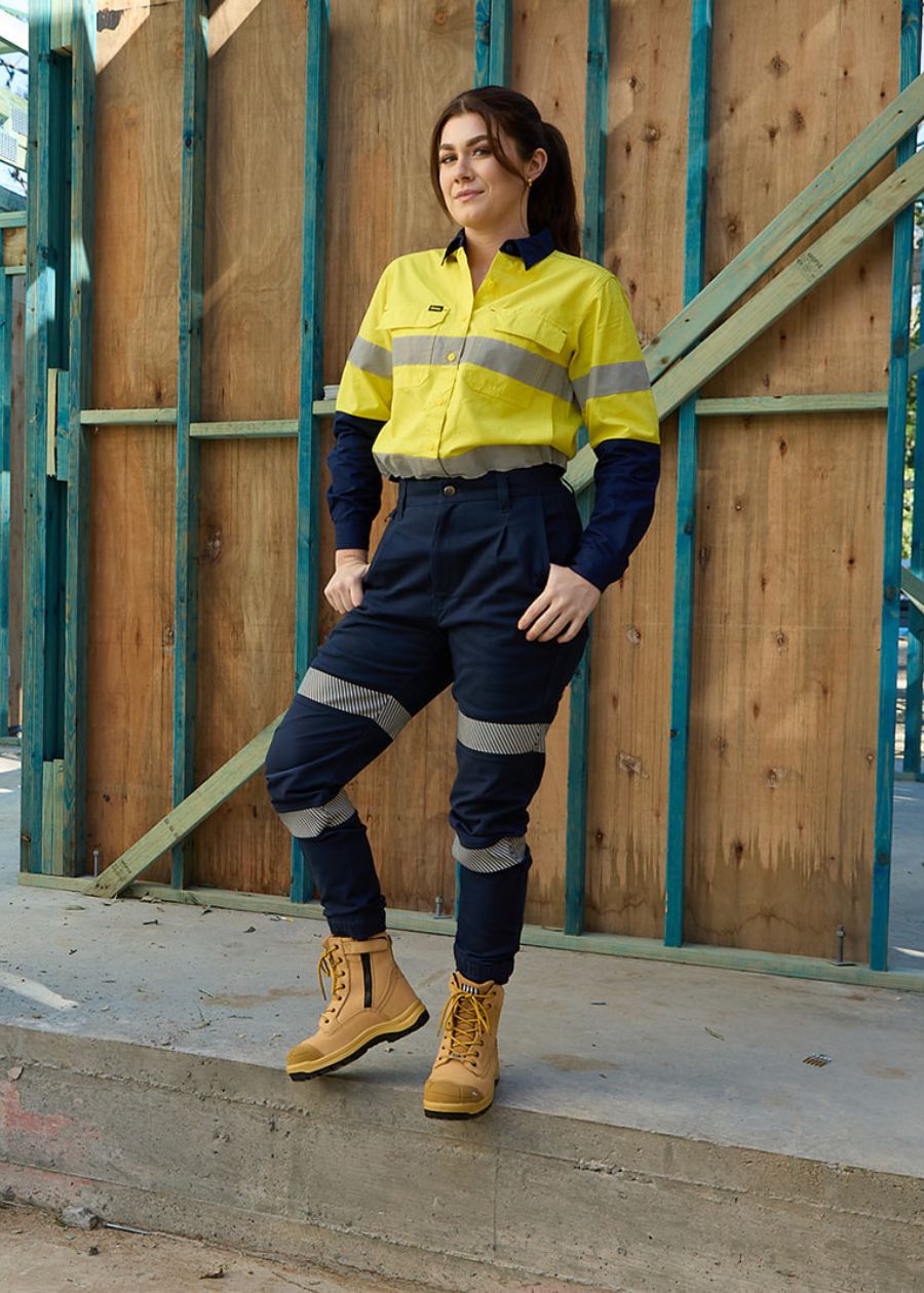 Woman on work site wearing high waisted, work pants featuring two reflective strips.